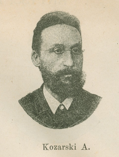Portret mężczyzny z brodą, lekko z profilu. Ma krótką fryzurę, zaczesane do  tyłu włosy, wysokie czoło. Twarz poważna, na nosie okulary z małymi owalnymi oprawkami. Mężczyzna ma na sobie ciemny surdut i koszulę w białym kołnierzykiem. Pod portretem podpis: Kozarski A.