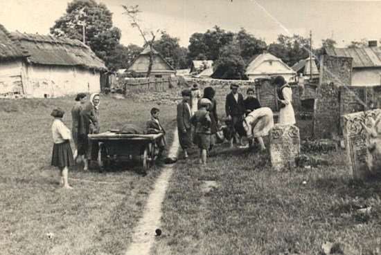 Grupa Żydów na cmentarzu za wsią, widoczny wóz z ciałem ubranym w specjalne pogrzebowe szaty i macewy.