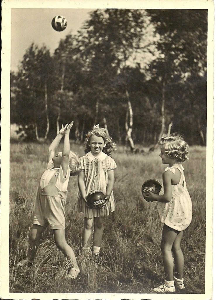 Troje dzieci gra latem w piłkę na łące. Stroje z początków 20 wieku.