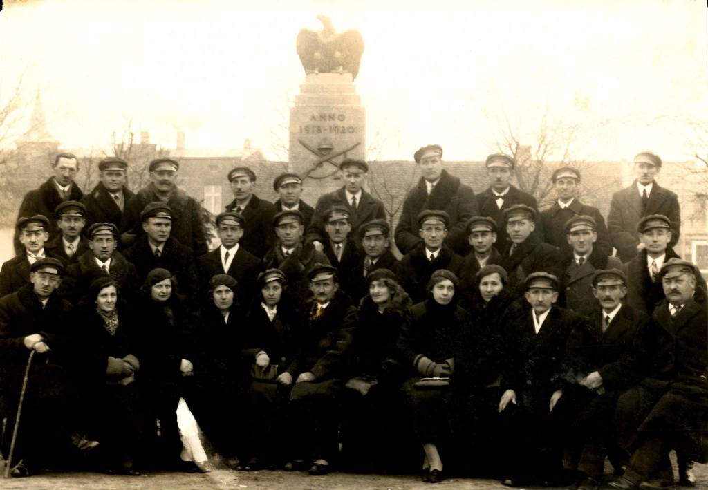 Na zdjęciu grupa kilkunastu osób ze związku Polskiej Organizacji Wojskowej pozuje na tle pomnika niepodległości. Na postumencie figura orła.